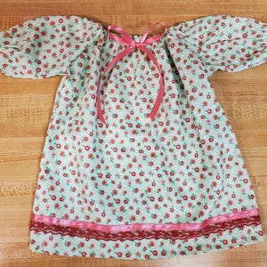 May include: A light blue floral print dress with short, puffed sleeves and a pink ribbon tie at the neckline. The dress features a pink lace trim at the hemline, creating a vintage aesthetic.