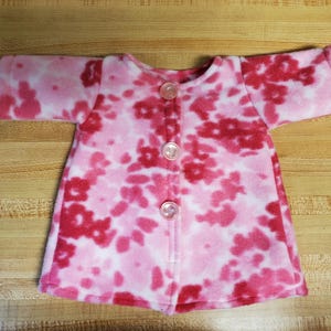 May include: A pink and red fleece jacket with a floral pattern and five pink buttons down the front.