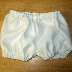 May include: White cotton baby bloomers with elastic waistband and leg openings.