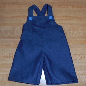 May include: Dark blue denim dungarees with two blue buttons on the straps.