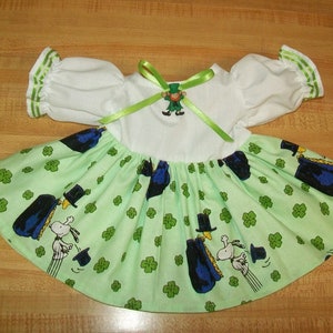 May include: A green and white dress with a shamrock print and a leprechaun charm. The dress has a white bodice and a green skirt with a gathered ruffle.