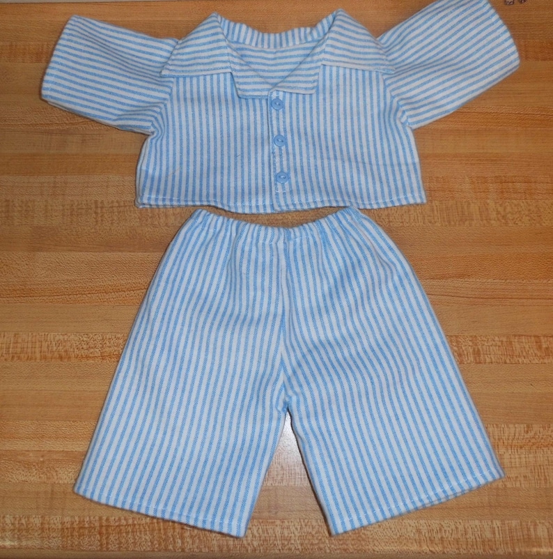 May include: A blue and white striped pyjama set. The top has short sleeves and a button-down front. The matching shorts have an elasticated waistband. The fabric is soft and lightweight, suitable for sleepwear.