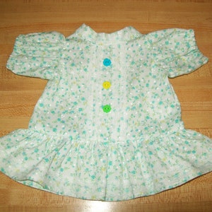 Puede incluir: Un vestido blanco con estampado floral verde y tres botones de colores en la parte delantera.