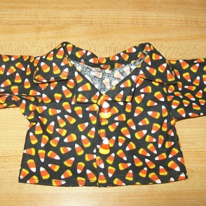 May include: A black button-up shirt with a candy corn print. The shirt has a collar and long sleeves. The buttons are orange and white candy corn.