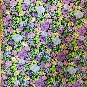 May include: A close-up of a fabric with a floral design. The pattern is composed of various flowers in shades of purple, blue, and white, set against a dark green backdrop. Green leaves are scattered throughout, creating a detailed and colourful textile.