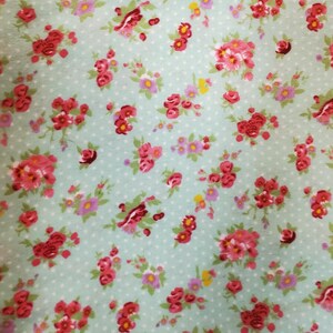 May include: A floral fabric with a repeating pattern of red and pink roses, small purple flowers, and green leaves. The design is set against a light blue backdrop with small white polka dots.
