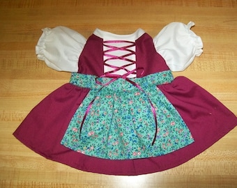 Puede incluir: Un vestido de muñeca con corpiño color burdeos intenso, mangas abullonadas blancas y detalle de cordones con cinta. La falda incluye un panel de delantal turquesa adjunto decorado con un estampado floral pequeño en tonos rosa, azul y verde.