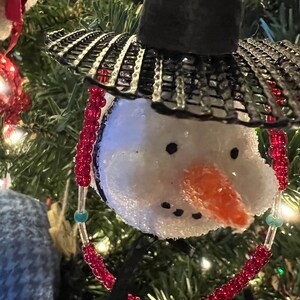 K&ouml;nnte beinhalten: Ein wei&szlig;er Schneemann-Anh&auml;nger mit einem schwarzen Hut und roten und t&uuml;rkisfarbenen Perlen. Der Schneemann hat eine Karottennase und schwarze Augen.