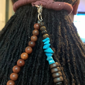 May include: A brown fabric hair tie with a silver clip attached to a beaded hair accessory. The beads are brown wood and turquoise blue.