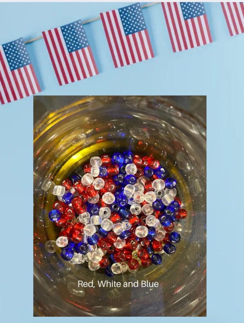 May include: A glass jar filled with red, white, and blue beads. Above the jar, small American flags are strung together. The text "Red, White and Blue" is at the bottom of the jar. The image has a patriotic theme.