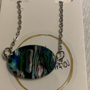May include: A silver chain necklace with a green, blue, and purple abalone shell pendant. The pendant is oval shaped and has a natural iridescent sheen.