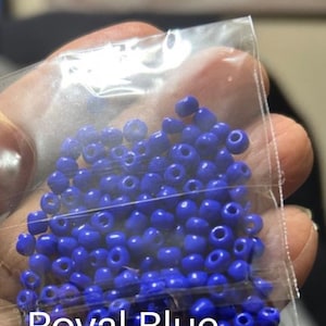 May include: A clear plastic bag filled with royal blue seed beads. The beads are small, round, and have a hole through the center. The text "Royal Blue" is printed in white at the bottom of the bag. These beads are ideal for jewelry making and crafts.
