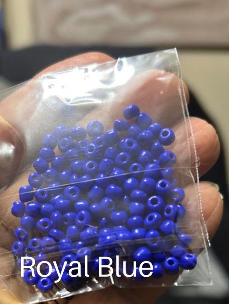 May include: A clear plastic bag filled with royal blue seed beads. The beads are small, round, and have a hole through the center. The text "Royal Blue" is printed in white at the bottom of the bag. These beads are ideal for jewelry making and crafts.