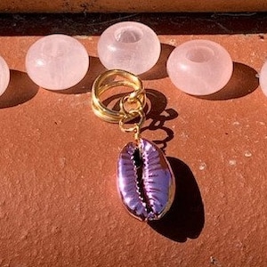 May include: A gold charm with a purple seashell pendant hangs from a gold chain. The charm is surrounded by five pink rose quartz beads.