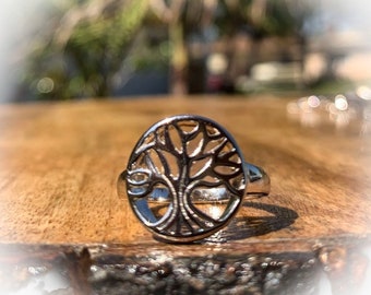 May include: A silver ring with a tree of life design. The ring is on a wooden surface.