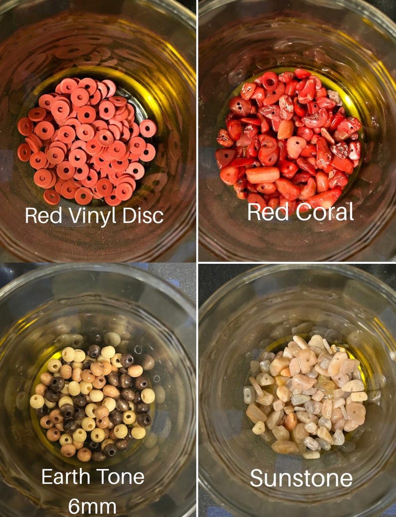 May include: Four glass jars filled with beads and stones. The jars contain red vinyl discs, red coral, earth tone 6mm beads, and sunstone. Text on the jars reads "Red Vinyl Disc", "Red Coral", "Earth Tone 6mm", and "Sunstone".