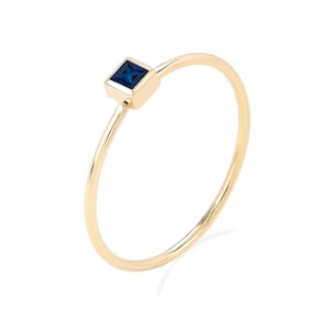 Op de afbeelding: Een delicate gouden ring met een kleine vierkante blauwe edelsteen.