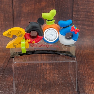 May include: A yellow, red, orange, blue, and green 2000 Walt Disney World Millennium Celebration clock figurine. The clock features Mickey Mouse, Donald Duck, and Goofy.