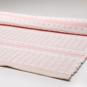 Puede incluir: Una alfombra tejida a rayas rosa y blanca con un patr&oacute;n texturizado. La alfombra est&aacute; enrollada y los bordes son visibles.