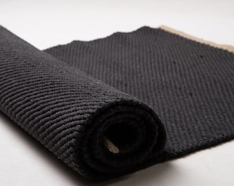 May include: A rolled up black rug with a textured surface. The rug is made of a thick, woven material and has a natural, earthy feel.