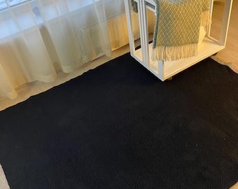 May include: A black and beige area rug with a textured surface. The rug is placed on a wooden floor.