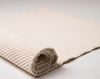 May include: A cream-colored, woven rug rolled up. The rug has a textured, ribbed pattern.