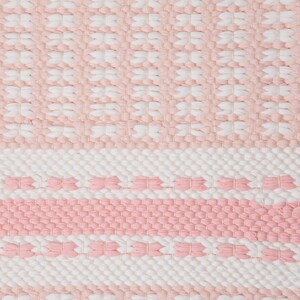 Puede incluir: Una alfombra tejida de color rosa y blanco con un patr&oacute;n geom&eacute;trico. La alfombra tiene una superficie texturizada y est&aacute; hecha de fibras naturales suaves.
