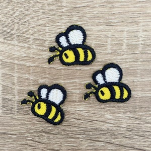 May include: Three yellow and black bee embroidered patches on a wooden background.