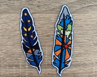 Könnte beinhalten: Zwei gestickte Bügelbilder in Form von Federn. Eine Feder ist blau mit gelben Sternen und einem Halbmond. Die andere Feder ist blau, orange und grün mit einem Sonnendesign.