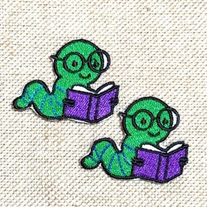 May include: Two embroidered patches featuring a green worm wearing glasses and reading a purple book. The worm has a green and blue striped body. The patches are on a beige fabric background.