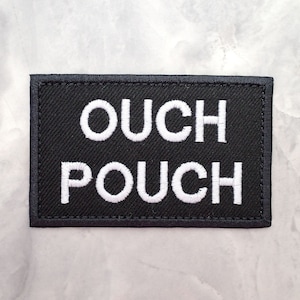 Può includere: Toppa in tessuto nero con testo ricamato bianco che recita "OUCH POUCH".
