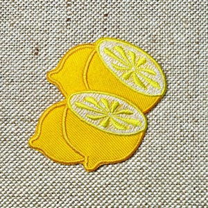 Può includere: Due toppe di limone in feltro giallo con dettagli ricamati. I limoni sono cuciti insieme e hanno una superficie testurizzata.