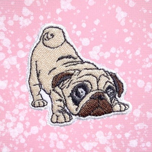 May include: Embroidered patch of a brown and white pug dog with its head turned to the side. The pug is looking at the viewer with its tongue sticking out. The patch is on a pink background with white speckles.