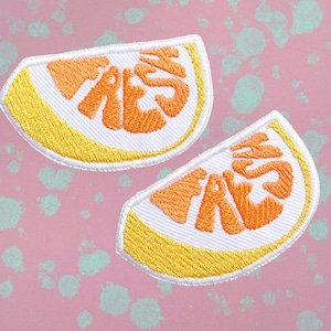 Puede incluir: Dos parches bordados para planchar con forma de rodajas de limón con la palabra "FRESH" en letras naranjas sobre fondo blanco.