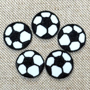 May include: Five black and white soccer ball patches arranged in a circular pattern. Each patch features a classic soccer ball design with black pentagons and white hexagons. The patches are embroidered with a textured fabric.