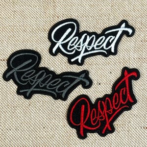 Op de afbeelding: Drie geborduurde patches met het woord "Respect" in een sierlijk lettertype. Eén patch heeft witte letters op een zwarte achtergrond, een andere grijze letters op zwart en de derde rode letters op zwart.