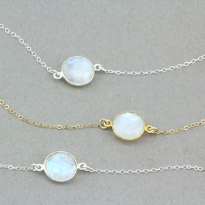 Puede incluir: Tres delicados collares con cadenas de plata y oro y colgantes ovalados de piedra lunar.