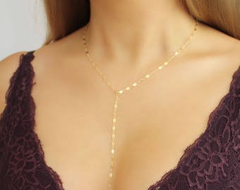 Könnte beinhalten: Eine goldene Kettenkette mit einem langen, baumelnden Anhänger. Die Kette wird von einer Person mit einem burgunderfarbenen Spitzenoberteil getragen.