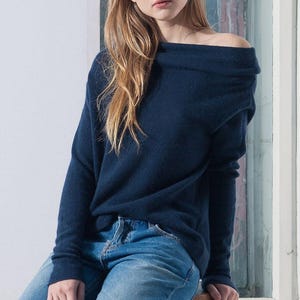 Peut inclure: Un pull bleu marine à épaules dénudées avec des manches longues. Le pull est fait d'un tissu doux et confortable et a une coupe décontractée.