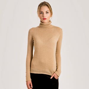 Peut inclure: Une femme porte un pull à col roulé beige et un pantalon en velours noir. Le pull à manches longues a une texture côtelée. Le pantalon est large et légèrement brillant. La femme porte des chaussures argentées.