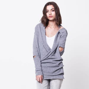 May include: A gray sweater with a wrap style and elbow-length sleeves. The sweater has a V-neck and is worn with light gray jeans and black ankle boots.