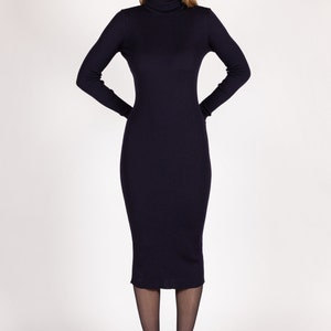 Op de afbeelding: Een lange, donkerblauwe rolkraagjurk met een geribbelde textuur. De jurk is aangesloten en valt tot op de knie&euml;n. Het model draagt zwarte panty's en zwarte plateauhakken.