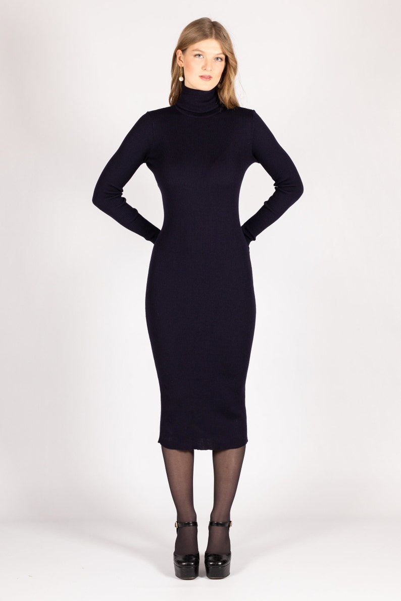 Op de afbeelding: Een lange, donkerblauwe rolkraagjurk met een geribbelde textuur. De jurk is aangesloten en valt tot op de knie&euml;n. Het model draagt zwarte panty's en zwarte plateauhakken.