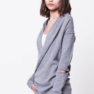 May include: A gray knitted cardigan with a draped neckline and a distressed detail on the sleeves.