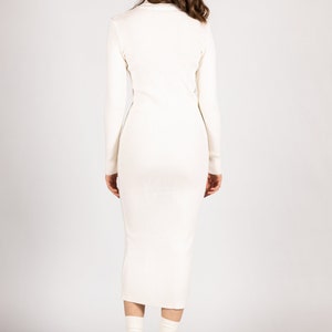 K&ouml;nnte beinhalten: Ein wei&szlig;es geripptes Midikleid mit langen &Auml;rmeln. Das Kleid ist figurbetont und hat einen leicht ausgestellten Rock. Das Model tr&auml;gt das Kleid mit schwarzen Plateau-Heels.