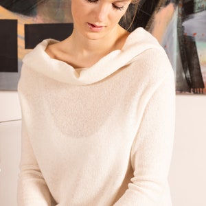 May include: A white cowl neck sweater with long sleeves. The sweater is made of a soft, lightweight fabric.