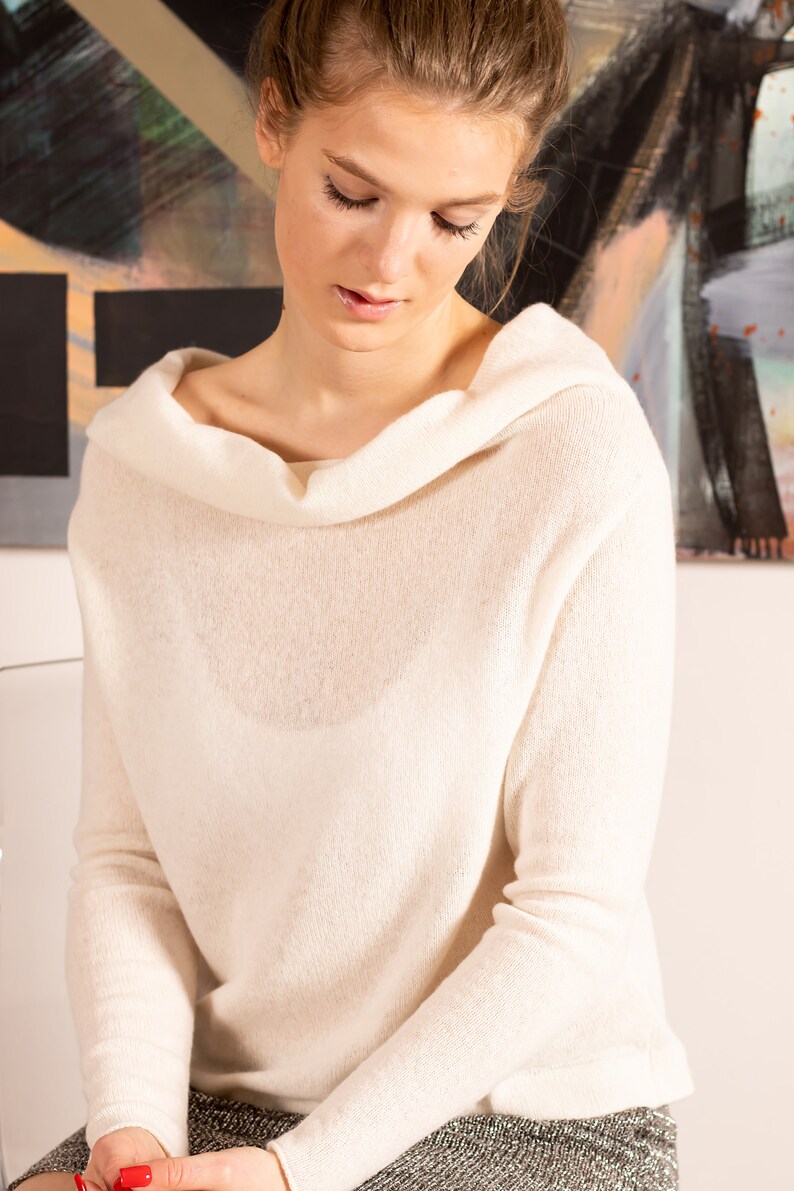 May include: A white cowl neck sweater with long sleeves. The sweater is made of a soft, lightweight fabric.