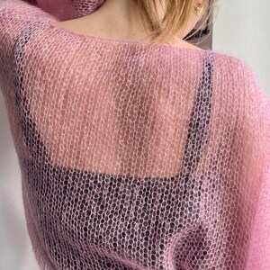 Puede incluir: Un su&eacute;ter rosa claro de tejido abierto. El su&eacute;ter est&aacute; hecho de un material transparente y delicado, con un ajuste holgado y aireado. El su&eacute;ter se usa sobre una parte superior negra, creando un contraste de color y textura. El aspecto general es suave y femenino.