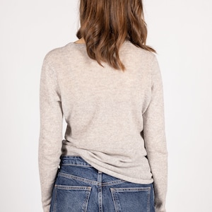 May include: A light gray long-sleeved sweater with a v-neck and a pair of blue denim jeans.