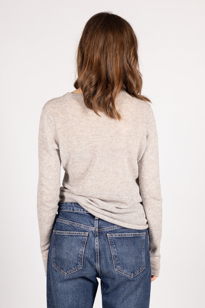 May include: A light gray long-sleeved sweater with a v-neck and a pair of blue denim jeans.